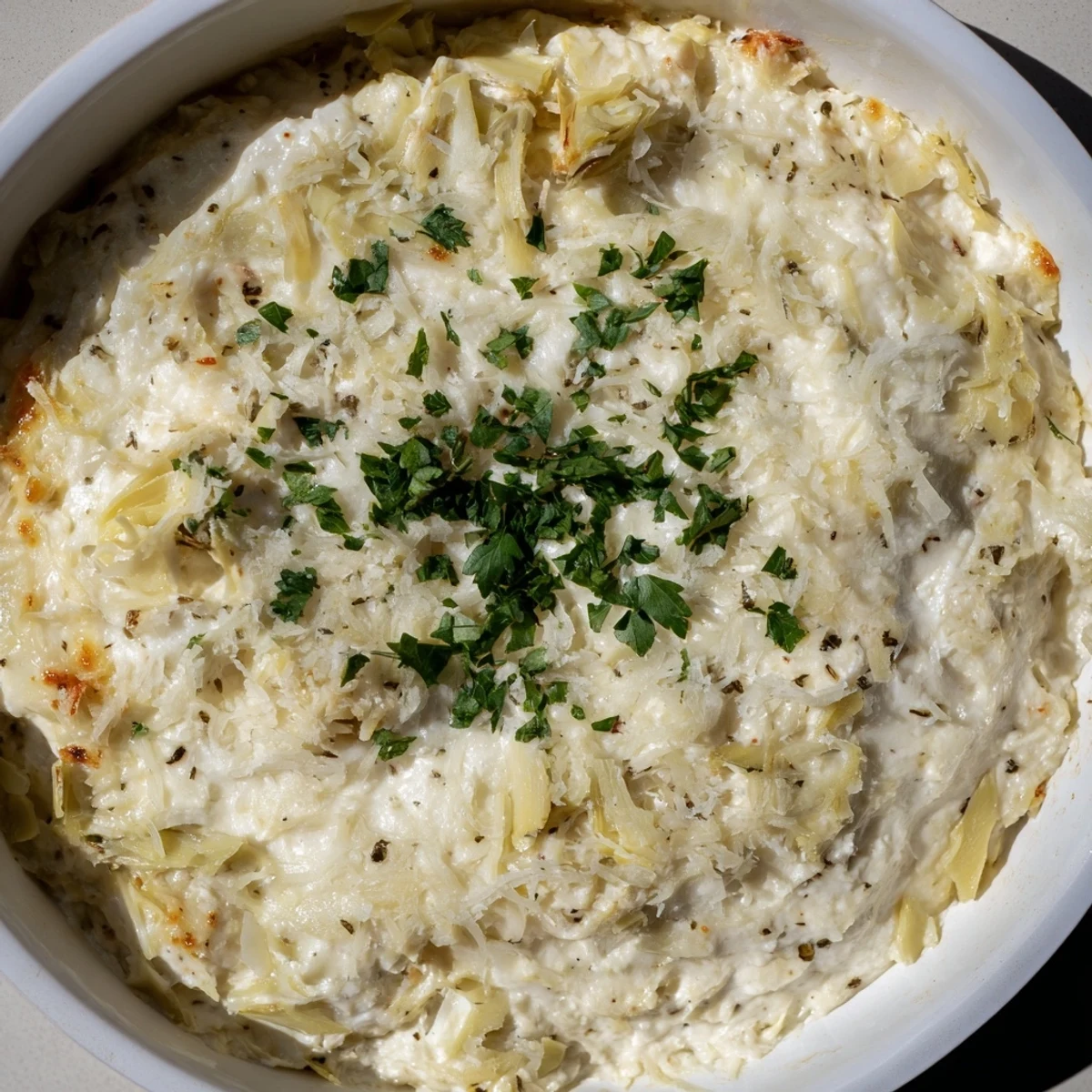 Savory Baked Artichoke Dip, bubbling from the oven, with a creamy base and artichoke pieces.