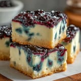 Creamy no-bake lemon blueberry cheesecake bars served chilled, visually swirled with fruit.