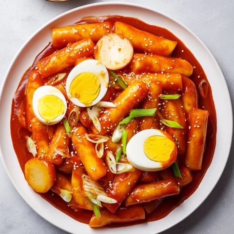 Steaming bowl of vibrant Korean Tteokbokki, with glistening rice cakes and perfectly cooked eggs.