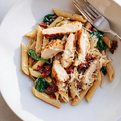 Top-down view of flavorful Tuscan Chicken Pasta with penne, spinach, and sun-dried tomatoes.