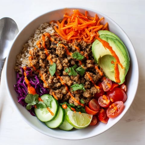 Delicious plant-based meat bowl drizzled with spicy mayo and surrounded by vibrant toppings.  