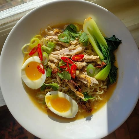 Close up shows flavorful Thai Miso Ramen with tender chicken, soft egg, and crispy shallots.