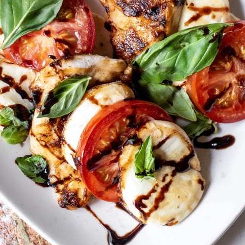A close-up of sizzling Caprese Chicken Skillet drizzled with balsamic glaze and garnished with fresh basil.