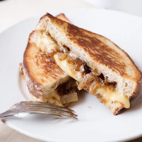 The sandwich rests on a wooden board beside a small bowl of tomato soup, perfect for dipping and enjoying a comforting lunch.  