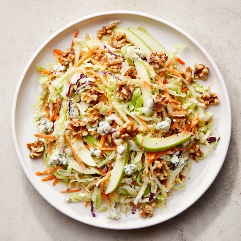 A close-up of finished Crunchy Apple & Walnut Slaw, showing glistening apples, walnuts, and creamy blue cheese.