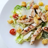 Grilled chicken strips on crisp romaine lettuce for a Yogurt Caesar Grilled Chicken Salad, featuring a creamy dressing and crunchy homemade croutons.